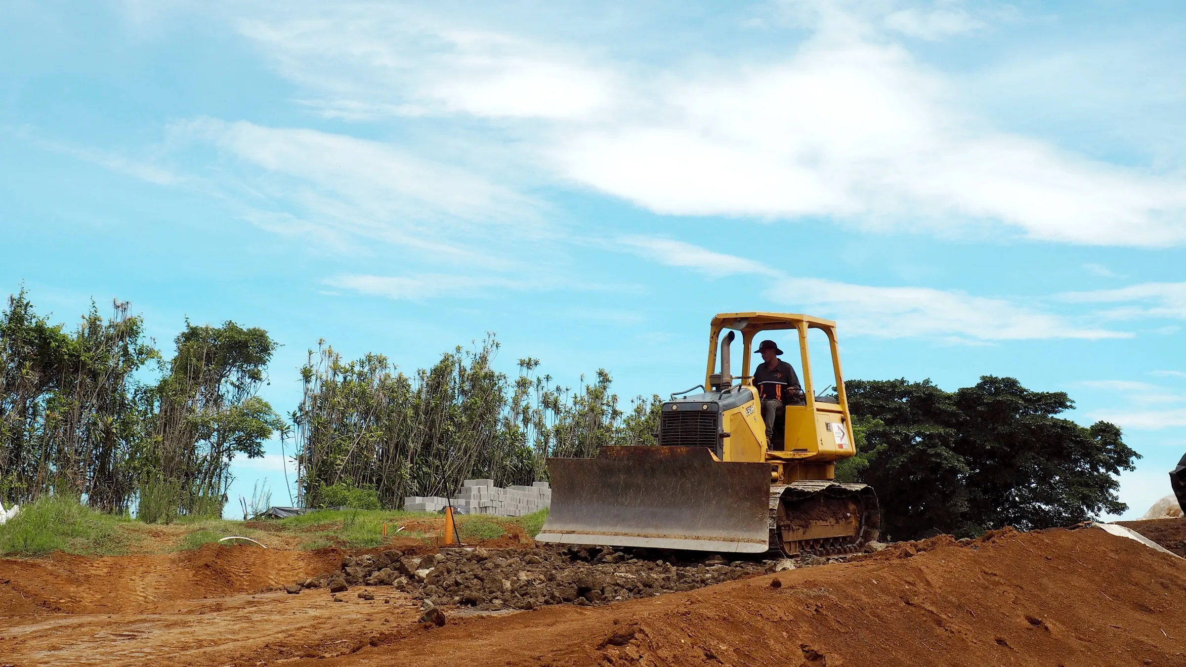A dozer grading red earth on a hilltop construction site under a bright blue Costa Rican sky